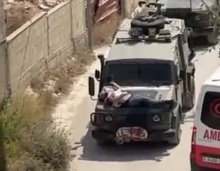 Ảnh chụp màn hình đoạn clip cho thấy một người đàn ông Palestine bị trói vào mui một xe quân sự Israel