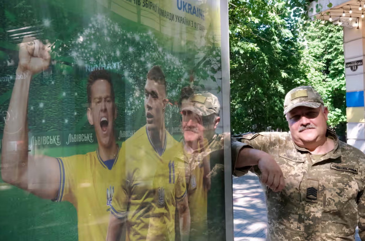 Một người lính đứng dựa vào biển quảng cáo Euro 2024 tại thành phố cảng Odessa, Ukraine. Đây là một trong số ít biển quảng cáo về Euro 2024 tại đường phố Odessa, vì chiến tranh gần như đã chiếm toàn bộ các thông điệp tuyên truyền trên phố - Ảnh: RICHARD MORGAN