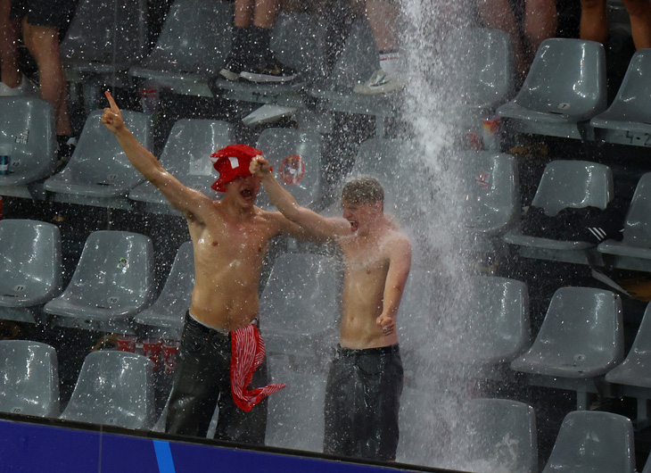 Hai cổ động viên Đan Mạch tranh thủ tắm mưa trong lúc trận đấu bị hoãn - Ảnh: REUTERS