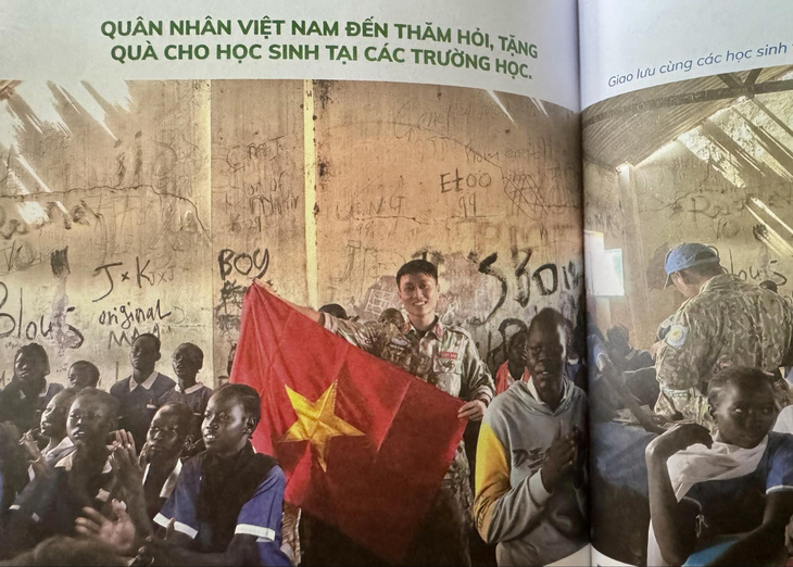 Hình ảnh anh Công bên lá cờ Việt Nam tại trường Prat khi anh đến thăm hỏi, tặng quà cho các em học sinh ở đây - Ảnh: chụp từ sách