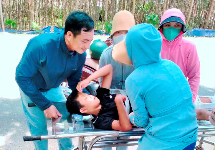 Cháu bé sau khi được anh Trần Anh Tuấn, cán bộ Phòng CSGT Công an Quảng Bình, cho tiền gọi xe cấp cứu thì được người dân hỗ trợ đưa lên xe cứu thương - Ảnh: LÊ NHÀN