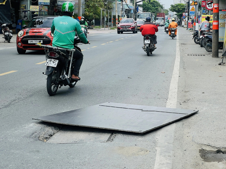 Tấm thép che miệng hố ga sụp lún nhưng nằm chỏng chơ như cái bẫy - Ảnh: XUÂN ĐOÀN