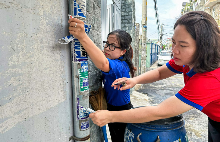 Cán bộ và người dân phường Thới An (quận 12, TP.HCM) chung tay bóc quảng cáo dán bậy ở trụ điện, tường nhà - Ảnh: GIAI THỤY