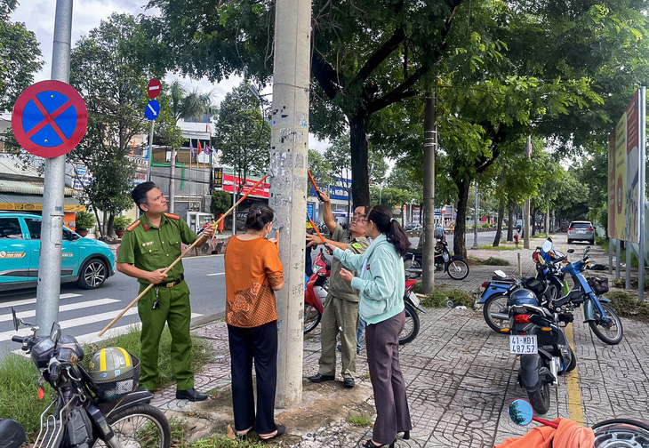 Người dân, công an phường, công an khu vực chung tay bóc quảng cáo dán bậy - Ảnh: GIAI THỤY