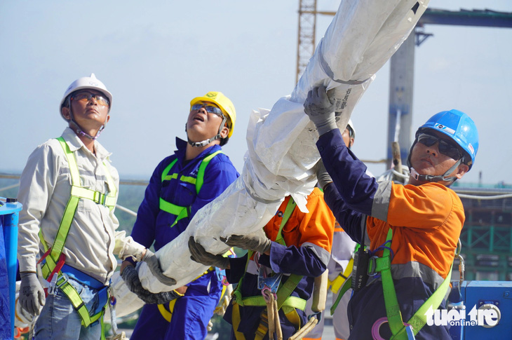 Các công nhân, kỹ sư đang tiến hành căng dây văng đầu tiên của cầu Rạch Miễu 2 - Ảnh: MẬU TRƯỜNG