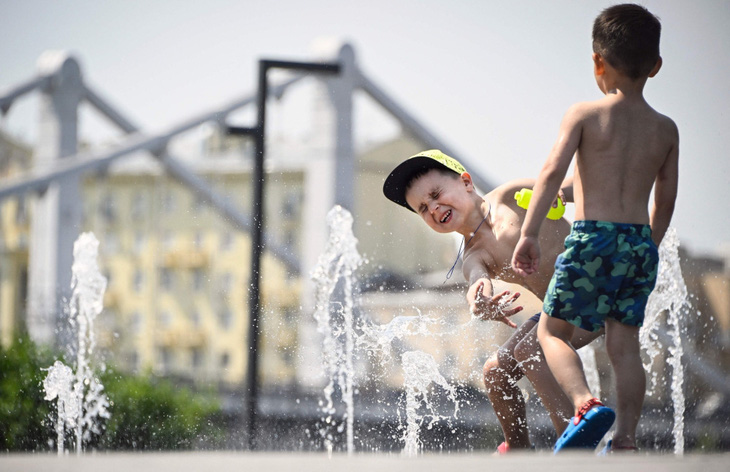 Trẻ em chơi đùa dưới đài phun nước trong nắng nóng ở trung tâm Mátxcơva vào ngày 3-7-2024 - Ảnh: AFP