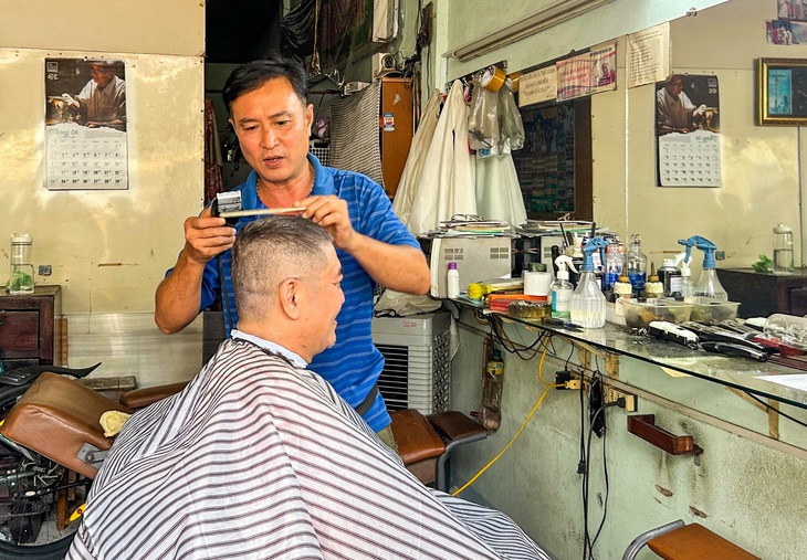 Chủ tiệm hớt tóc Nguyễn Văn Thắng đang hớt tóc cho khách tại khu chợ Ga - Ảnh: PHAN NGUYỄN QUỲNH TRÂM