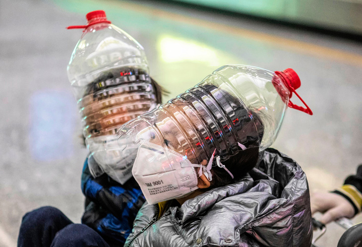Con nít vừa đeo khẩu trang, vừa mang thêm mặt nạ tự chế, làm từ vỏ chai nước, để “chống lại virus corona” ở ga đến của sân bay Quảng Châu, tỉnh Quảng Đông (Trung Quốc), ngày 1 tháng 2 năm 2020. Hình của Alex Plavevski (EPA / EFE).