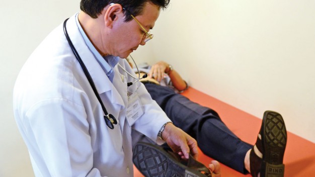 ThS.BS Bùi Quang Đi (Bệnh viện Hoàn Mỹ Sài Gòn) tự tay tháo dép cho một bệnh nhân lỡ mang dép khi nằm lên giường khám - Ảnh: Quang Định