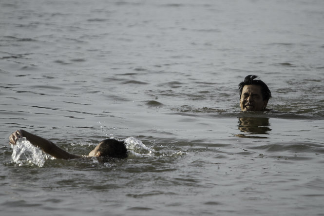 Một người lớn cố bơi vào gần bờ, trong khi một đứa bé đang bơi ra khu vực đó