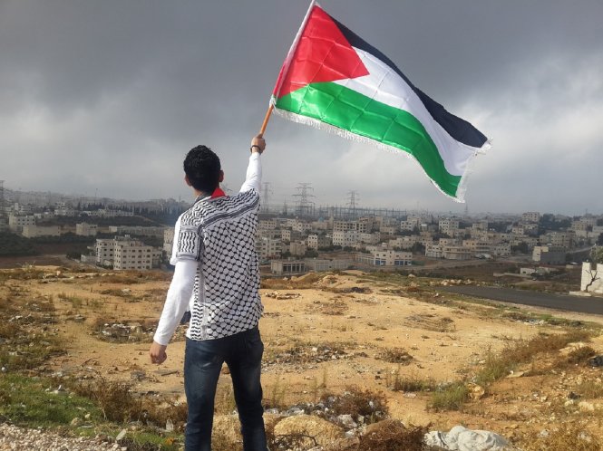 Một thiếu niên vô danh vẫy lá cờ Palestine trước một khu định cư của Israel tại Bờ Tây. Giấc mơ về một nhà nước Ả Rập thống nhất vẫn còn sức sống ở thế kỷ 21.-Ảnh: Wikimedia