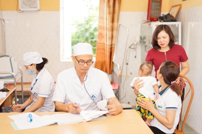 Bà Dương Thị Hồng (đứng) trao đổi với một bà mẹ tại điểm tiêm chủng. Ảnh: Thúy Anh