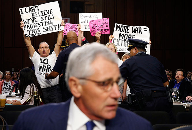 Những người phản đối chiến tranh giương các khẩu hiệu trong lúc ông Hagel ngồi vào ghế tại cuộc điều trần trước Ủy ban quân vụ Thượng viện ngày 16-9 về chính sách của Mỹ đối với Iraq, Syria và mối đe dọa IS - Ảnh: Reuters