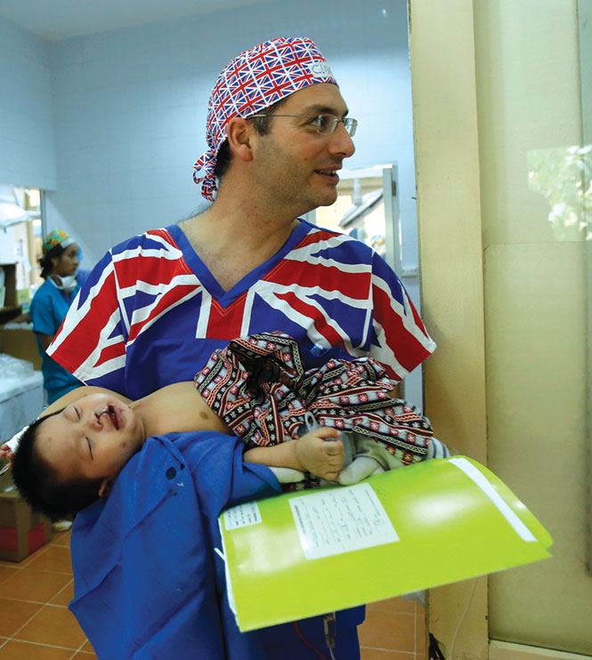 Bác sĩ Clive, người Anh, bế một em bé vừa phẫu thuật thành công sang phòng hồi sức