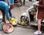 Người phụ nữ cán xe máy qua mẹt trái cây của chị bán hàng rong