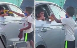 Bé trai ngồi trong ôtô lấy đồ chơi tặng cho cậu bé nghèo
